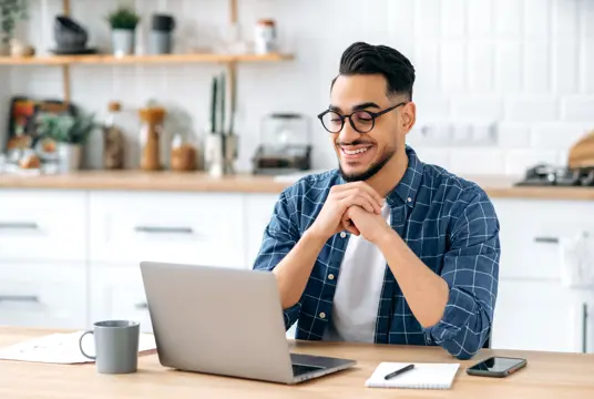 Glad man framför en dator vid köksbordet.