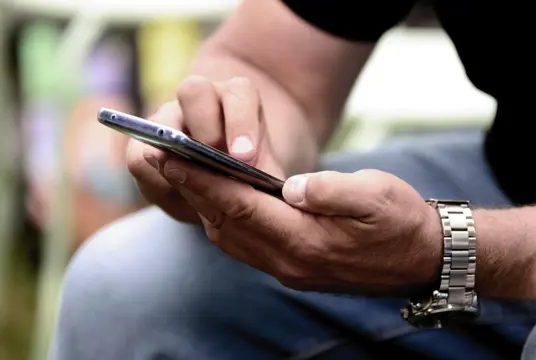 Närbild av händer som verkar tillhöra en man som surfar på en mobil.